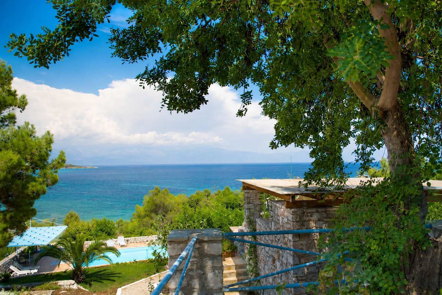 A stone structure with a pool, overlooking a clear blue sea and a distant coastline.