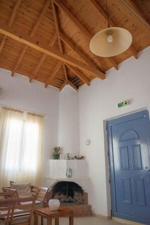 Quarto com teto de madeira, lareira, porta azul e janela com cortinas.
