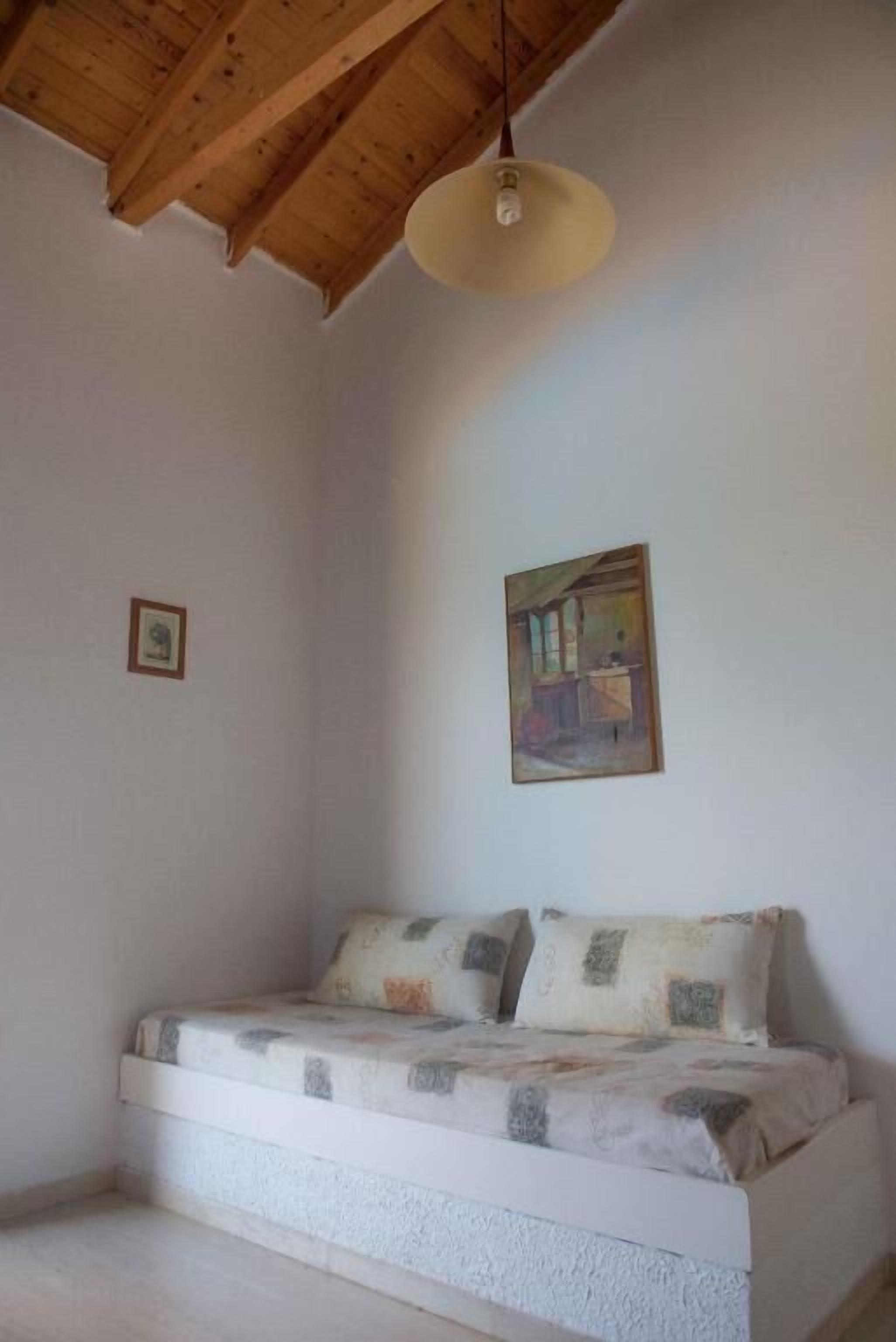 A room with a wooden ceiling, a bed with patterned bedding, and a single wall-mounted light fixture.