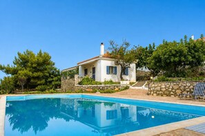 Uma casa com piscina, paredes de pedra e um jardim com árvores.