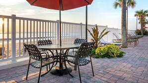 Eine Terrasse mit einem runden Tisch und Stühlen, einem roten Sonnenschirm und Blick aufs Meer.