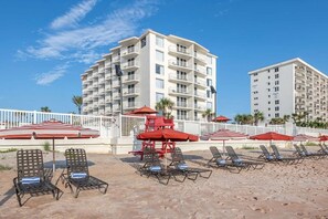 Een hotel aan het strand met meerdere balkons, ligbedden en parasols.