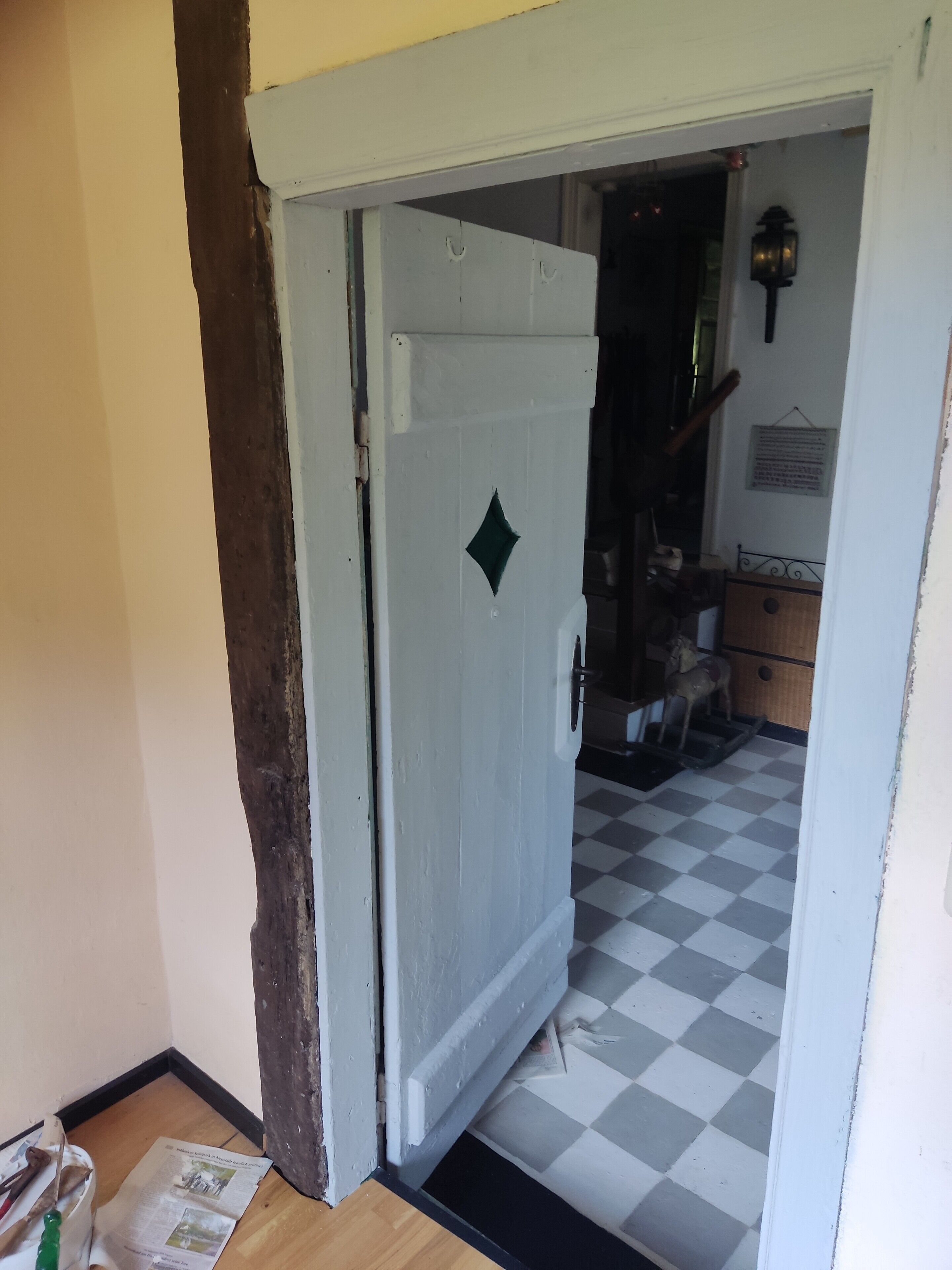 Ein Zimmer mit kariertem Boden, einer weißen Tür mit diamantförmiger Dekoration und einer wandmontierten Leuchte.