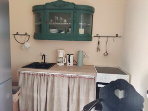 A compact kitchenette with a sink, coffee maker, kettle, and a stove. - "Knight’s Room" in Farmhouse on Riding Estate (Malente)