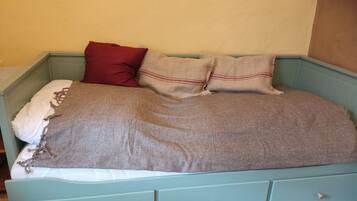Ein Bett mit einer grauen Decke, zwei Kissen und einem roten Kissen.