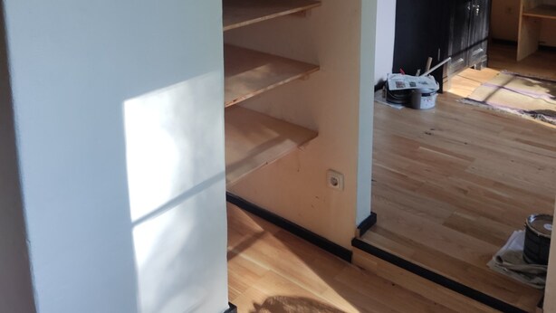 A room with a wooden floor, a white wall, and a black cabinet.
