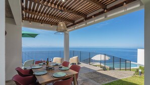 Un espace extérieur aménagé pour les repas, avec vue sur l’océan, une piscine et une pergola en bois.