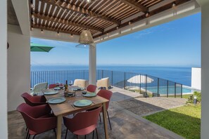 Ein Essbereich im Freien mit Blick auf den Ozean, einem Pool und einer Holzpergola.
