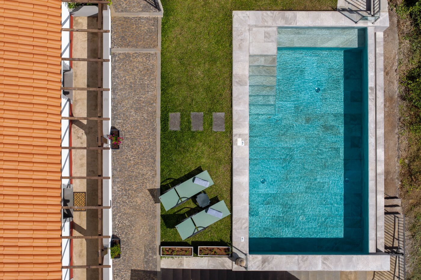 A rooftop pool with a clear blue water surface, surrounded by a stone deck and a grassy area with two lounge chairs.