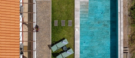 Una piscina en la azotea con superficie de agua azul cristalina, rodeada por una terraza de piedra y una zona ajardinada con dos sillones de descanso.