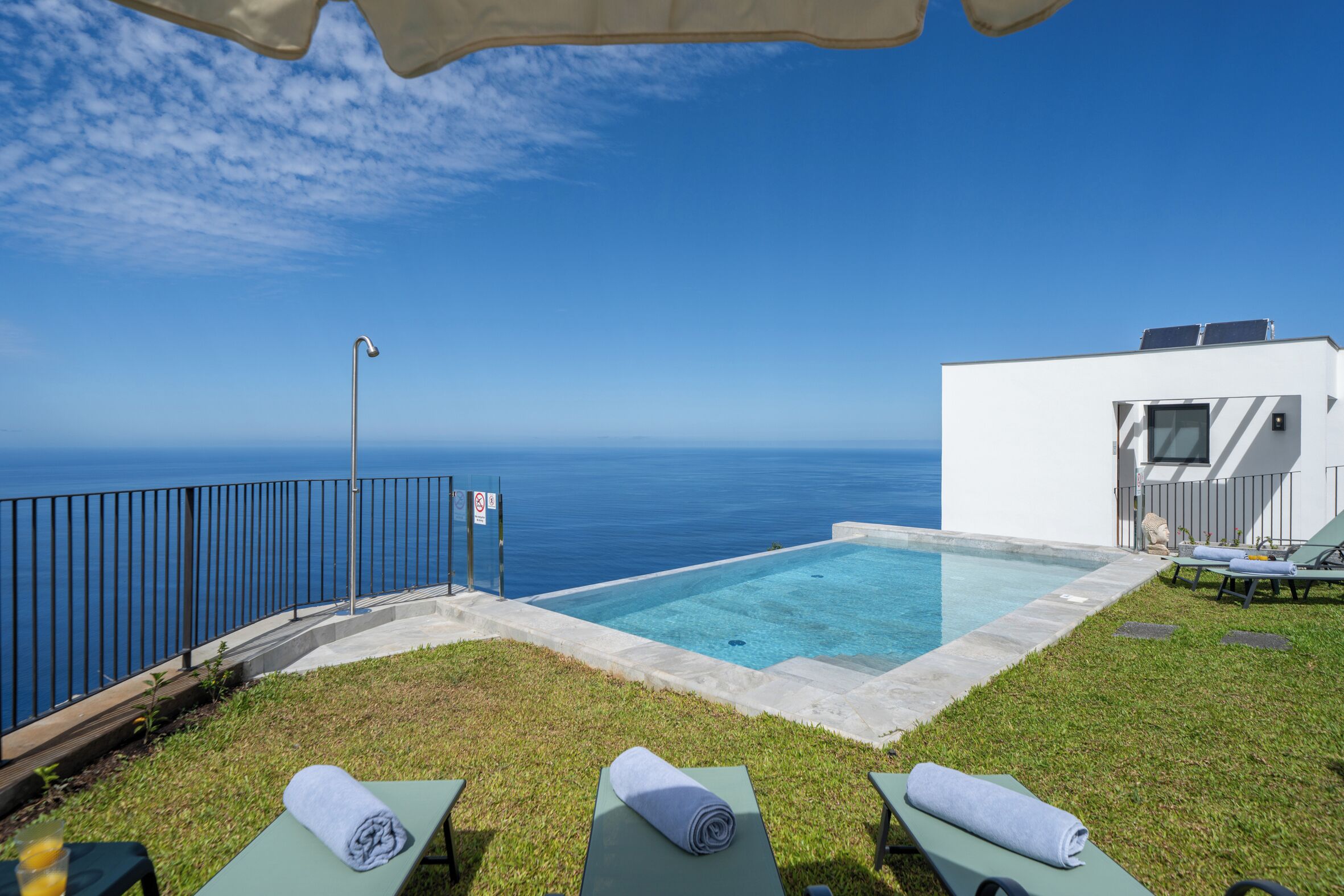A pool with a view of the ocean, a white building with solar panels, and lounge chairs with towels.