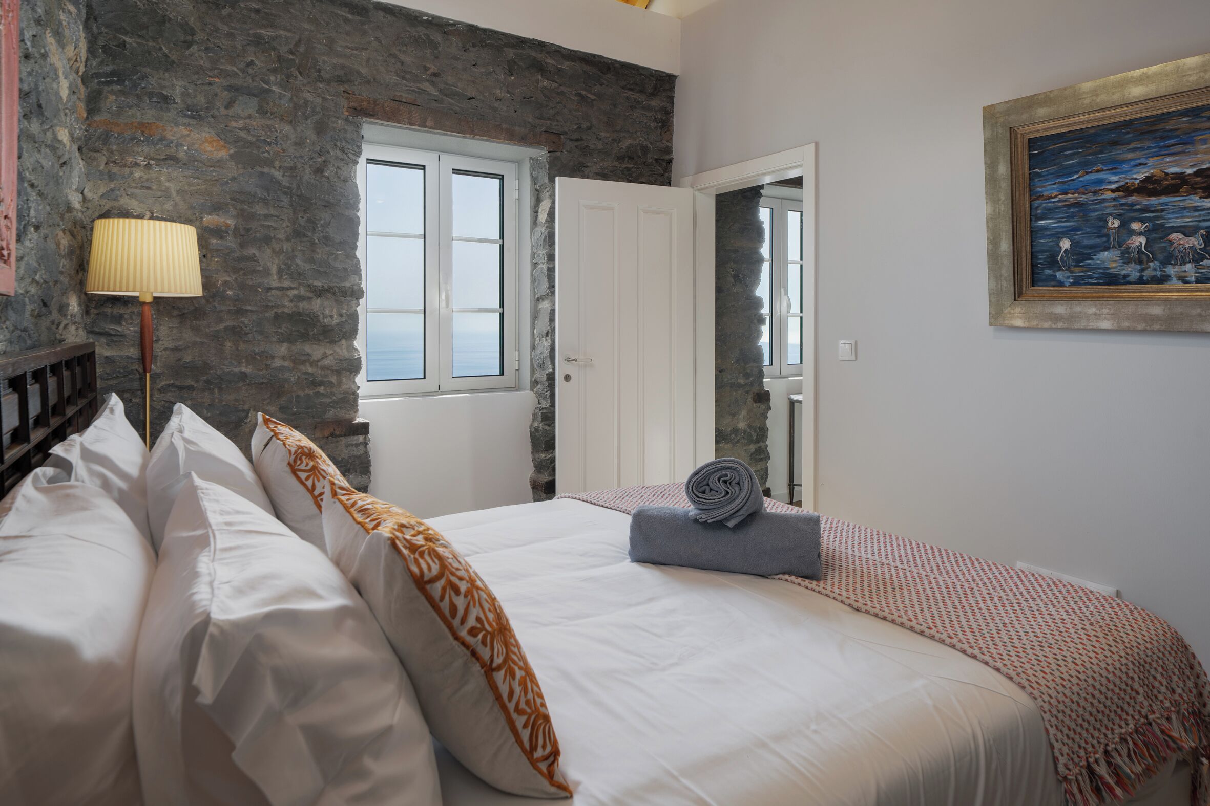 Ein Schlafzimmer mit Steinsturz, einem Bett mit weißen Leinen, einer Lampe und einem Gemälde.