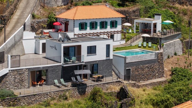 Une maison moderne à plusieurs étages, dotée d’une piscine, d’un espace salon extérieur et d’un mur de soutènement en pierre.