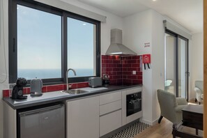 A modern kitchen with a dishwasher, a sink, and a stove. There is a window providing a view of the sea. - Tranquil with seaview|Ocean Hills Garden Studio (Faja Da Ovelha)