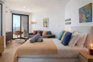 A modern bedroom with a large bed, a sofa, a desk, and a balcony. - Tranquil with seaview|Ocean Hills Terrace Studio (Faja Da Ovelha)