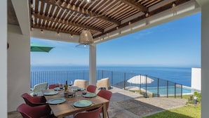 Un espace extérieur aménagé pour les repas, avec vue sur l’océan, une piscine et une pergola en bois.