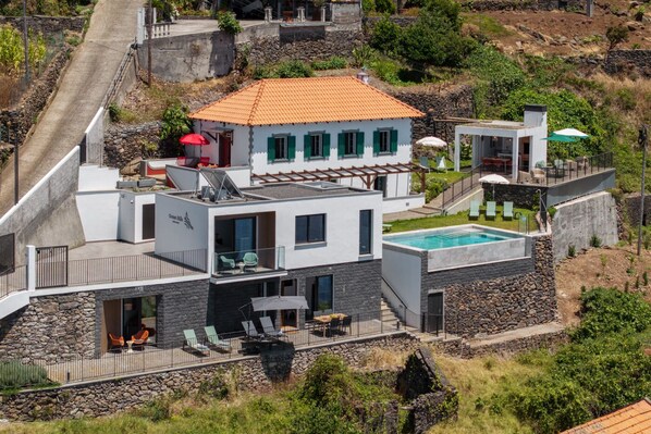 A modern multi-story house with a swimming pool, outdoor seating, and a stone retaining wall. - Tranquil with seaview|Ocean Hills Terrace Studio (Faja Da Ovelha)