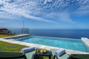 A pool with clear blue water, surrounded by lounge chairs and a view of the ocean. - Tranquil with seaview|Ocean Hills Terrace Studio (Faja Da Ovelha)