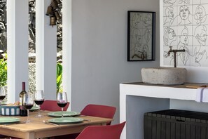 A dining area with a table set for two, a stone sink, and a framed abstract art piece on the wall. - Tranquil with seaview|Ocean Hills Terrace Studio (Faja Da Ovelha)