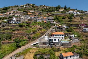 A hillside residential area with terraced houses, a prominent modern house with a flat roof, and a narrow road. - Tranquil with seaview|Ocean Hills Terrace Studio (Faja Da Ovelha)
