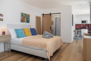 A modern bedroom with a bed, bedside table, and a nightstand with a lamp. - Tranquil with seaview|Ocean Hills Terrace Studio (Faja Da Ovelha)