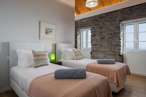A hotel room with two beds, a stone wall, and a framed picture on the wall. - Tranquil with seaview|Ocean Hills Balcony Studio (Faja Da Ovelha)