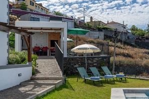 A modern outdoor seating area with a stone staircase leading to a covered patio, a pool, and a view of a hillside. - Tranquil with seaview|Ocean Hills Balcony Studio (Faja Da Ovelha)