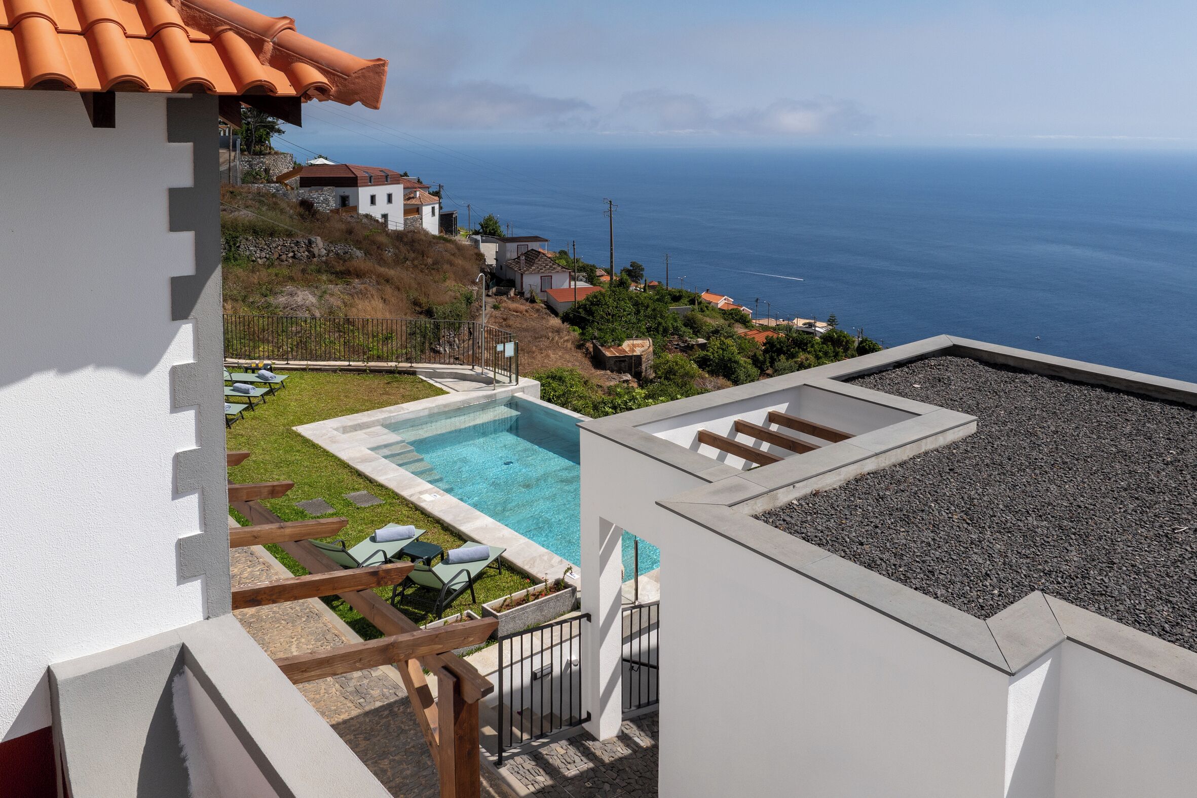 A residential property with a swimming pool, a view of the sea, and a hillside with houses.