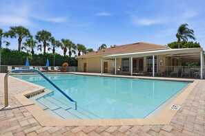 A rectangular swimming pool with a tiled deck surrounding it, a covered seating area with chairs, and palm trees in the background. - Villa With Lake and Golf Views on Public Arrowhead Golf Course (Naples)