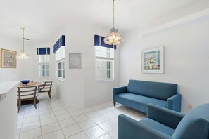 A modern living room with a blue sofa, a dining area with a table and chairs, and a kitchen visible in the background. - Villa With Lake and Golf Views on Public Arrowhead Golf Course (Naples)