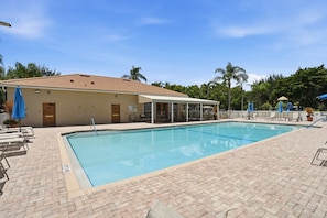 A swimming pool with a tiled deck, lounge chairs, and a covered seating area.