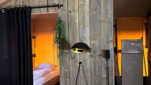A room with a wooden slat wall, a bed, a floor lamp, and a refrigerator. - Wilsumer Berge Resort - Glamfield Lodge 8 by Interhome (Wilsum)