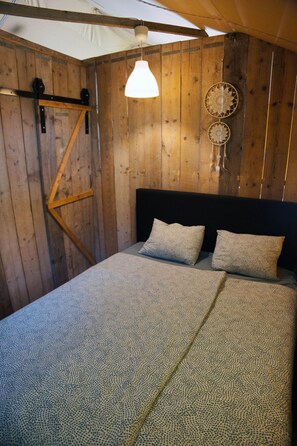Ein Zimmer aus Holz mit einem Bett, einer Hängelampe und einem Traumfänger an der Wand.
