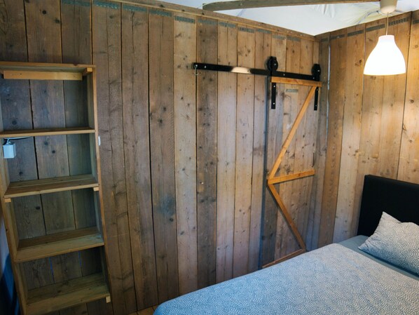 Un dormitorio con pared de madera, cama con colcha estampada, estante y lámpara colgante.