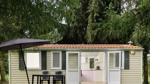 Een gelijkvloerse stacaravan met een terras, een tafel met stoelen en een schuifdeur naar een keuken.