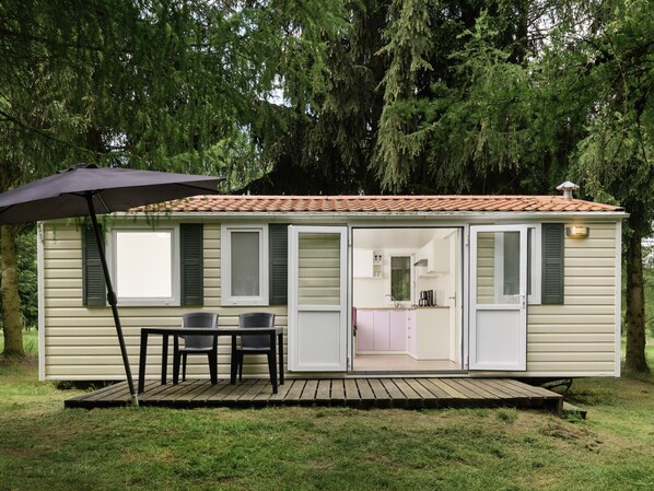 A single-story mobile home with a patio, a table with chairs, and a sliding door leading to a kitchen area.