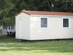A single-story mobile home with a red roof, white siding, and a small window.
