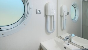 A bathroom with a round window, a mirror, a sink, and a hairdryer mounted on the wall. - Vacation home by Interhome (Osecná)