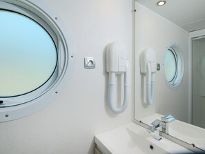 Ein Badezimmer mit einem runden Fenster, einem Spiegel, einem Waschbecken und einem an der Wand befestigten Föhn.