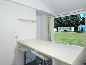 Ein modernes Zimmer mit weißem Schreibtisch, zwei Stühlen, einem fenster mit Vorhängen und Blick auf Mobilheime.