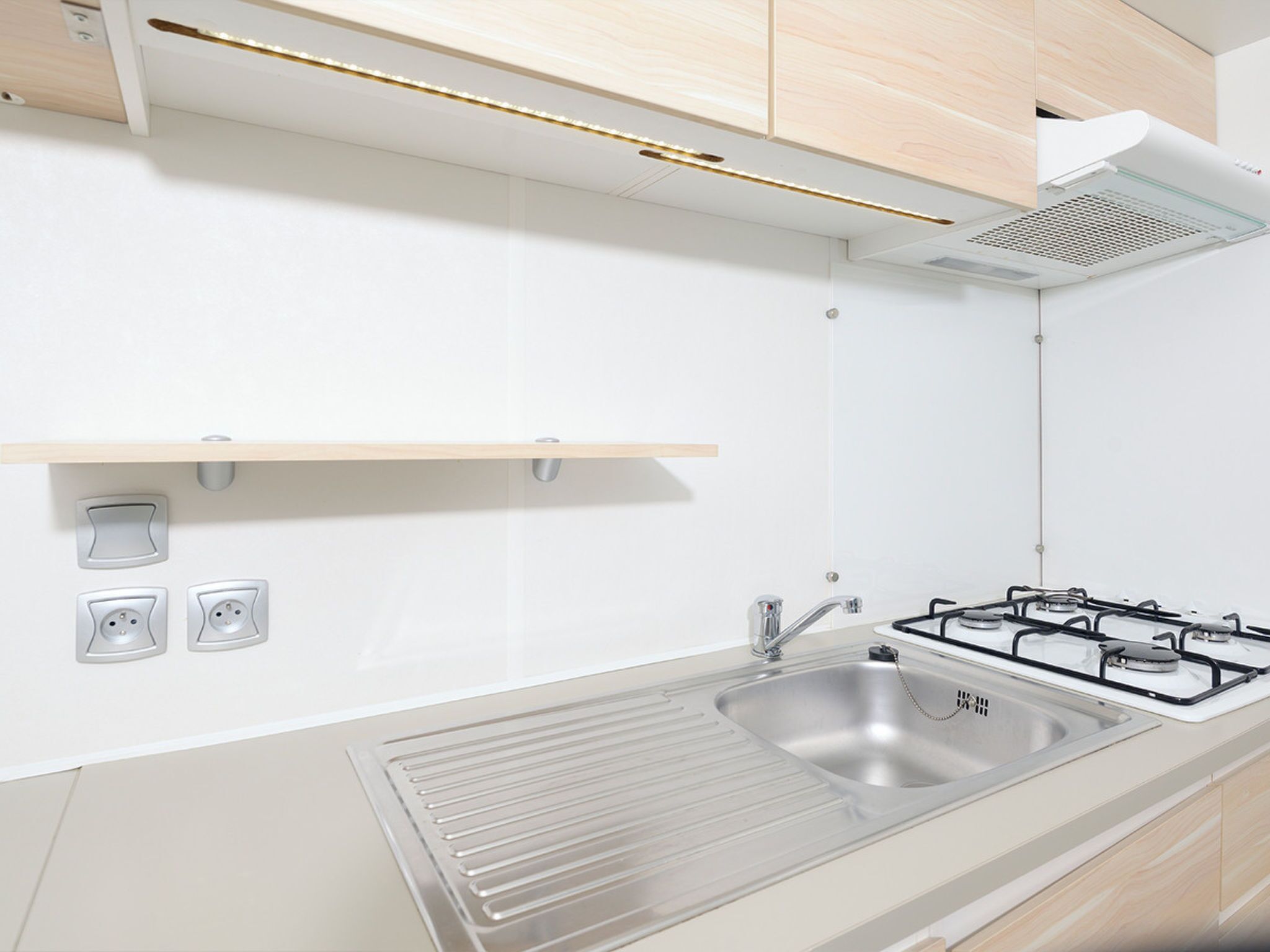 Una cocina moderna con un lavamanos de acero inoxidable, una estufa a gas y armarios de madera.