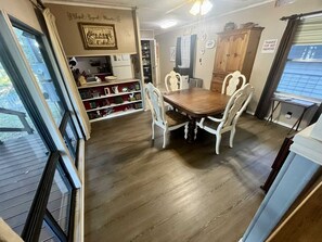 Ein Essbereich mit Holztisch und weißen Stühlen, ein Bücherregal und eine Küchenzeile mit Schränken und einem Kühlschrank.