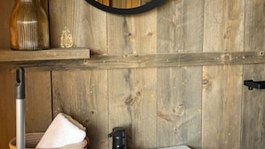 A bathroom with a white sink, a round mirror with a black frame, and a wooden wall. - Wilsumer Berge Resort - Glamfield Lodge Premium by Interhome (Wilsum)