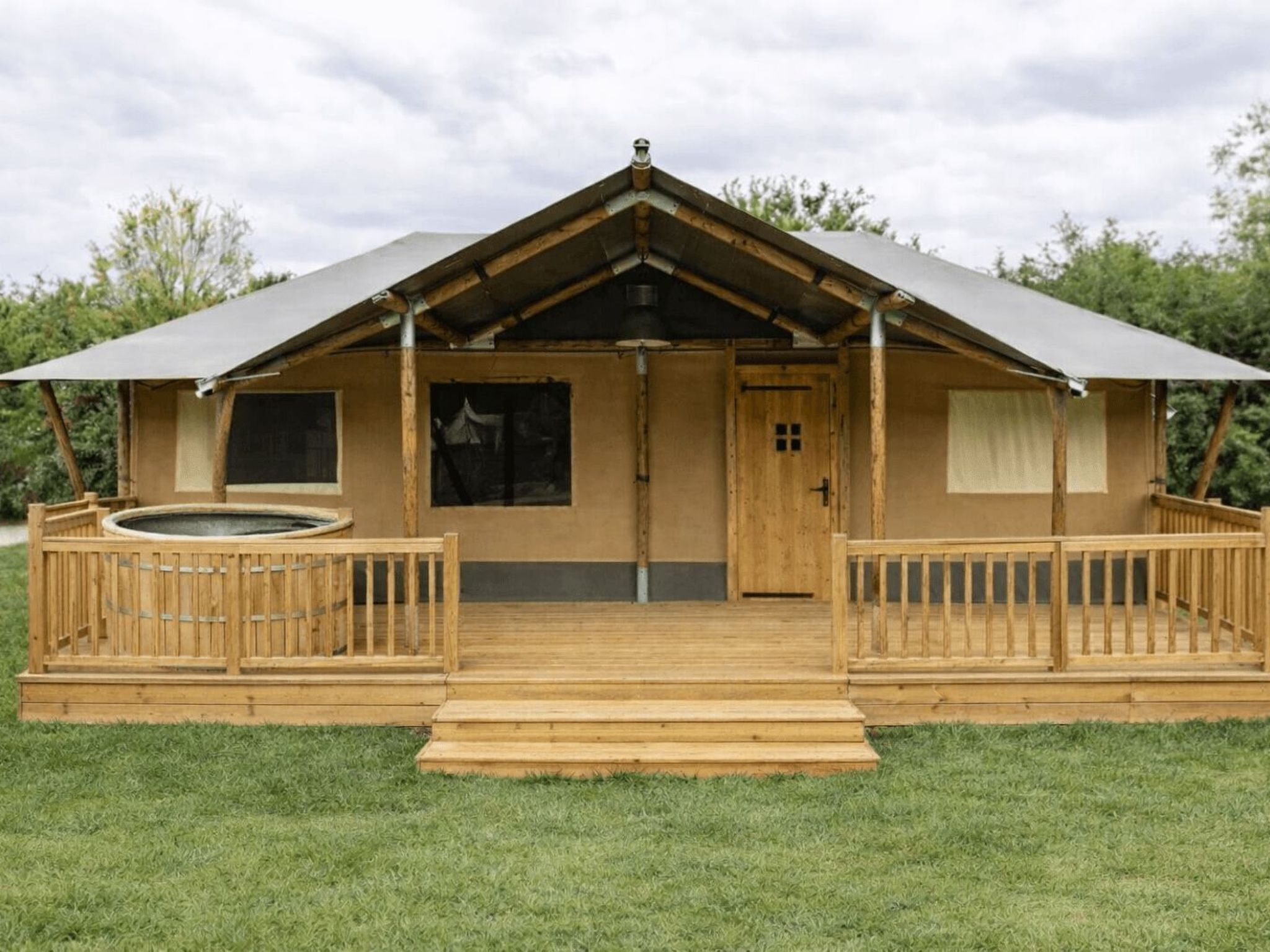 Una cabaña de madera con techo inclinado, un porche delantero y un jacuzzi.