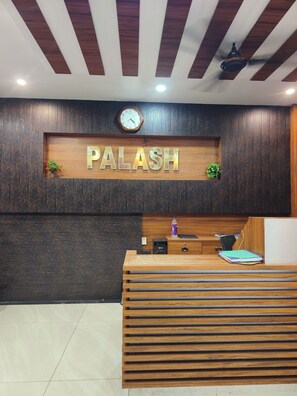 Un mostrador de recepción con detalles de madera, un reloj y un cartel que dice 'PALASH'.