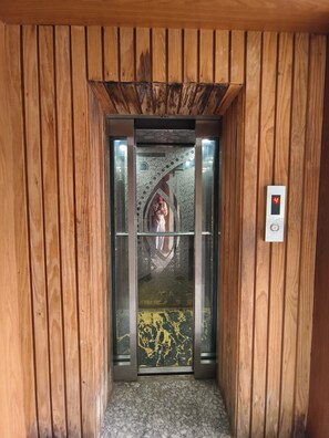 Un ascensor con pantalla digital mostrando el número 4, paneles de madera en las paredes y piso estampado.