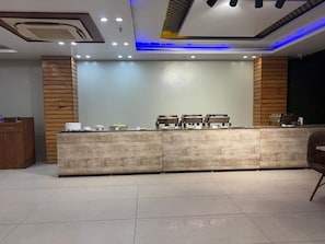 A reception area with a wooden reception desk, a counter with chairs, and a wall-mounted display. - HOTEL PALASH (Danapur)