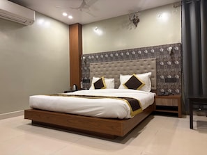 A modern bedroom with a large bed, a nightstand, a wall-mounted air conditioner, and a ceiling fan. - HOTEL PALASH (Danapur)