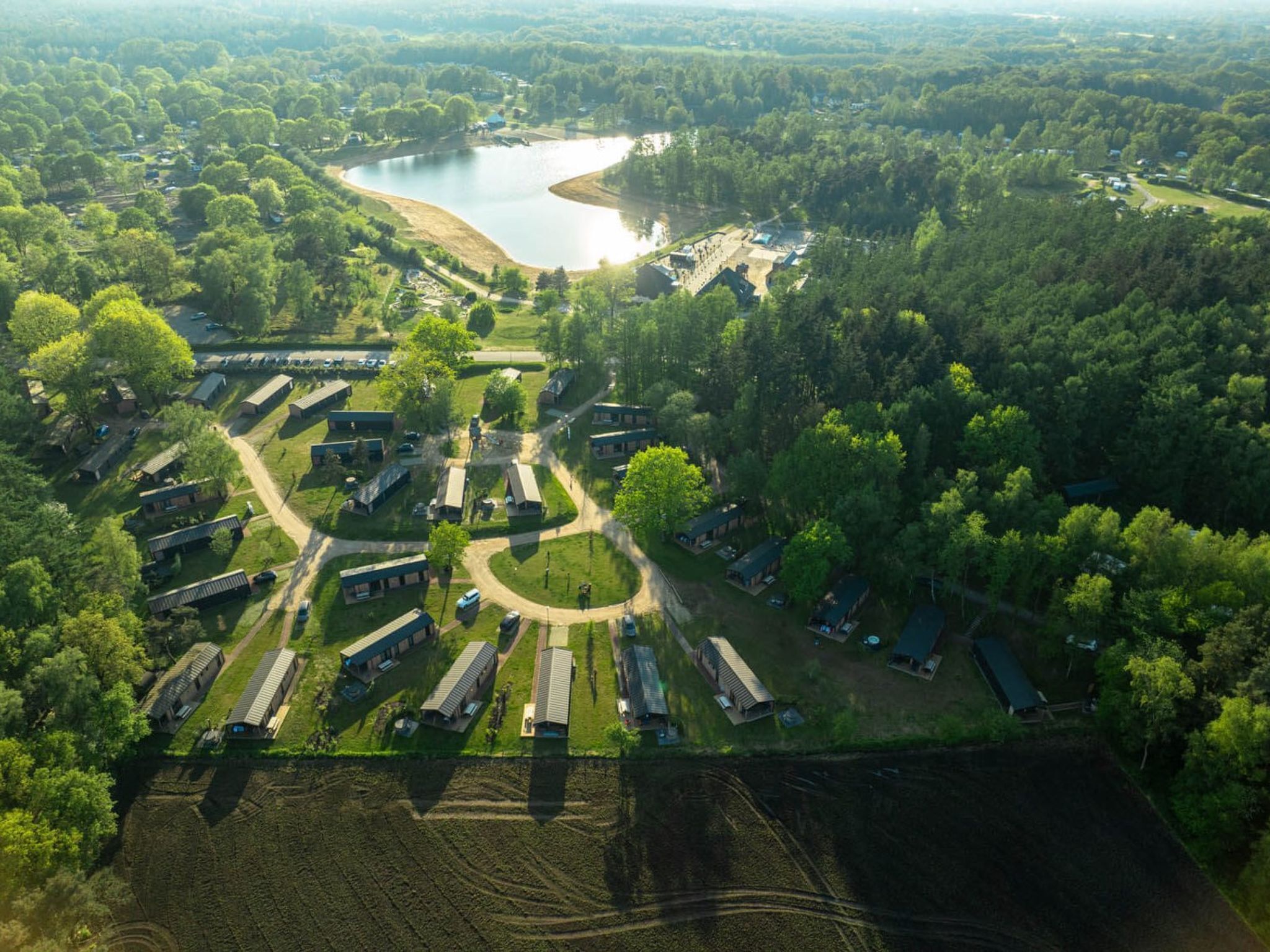 Vista aérea de un camping con varias cabañas, una zona de encuentro central y un lago.