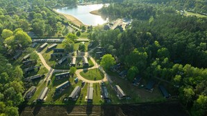 Een luchtbeeld van een camping met meerdere hutten, een centraal ontmoetingspunt en een meer.